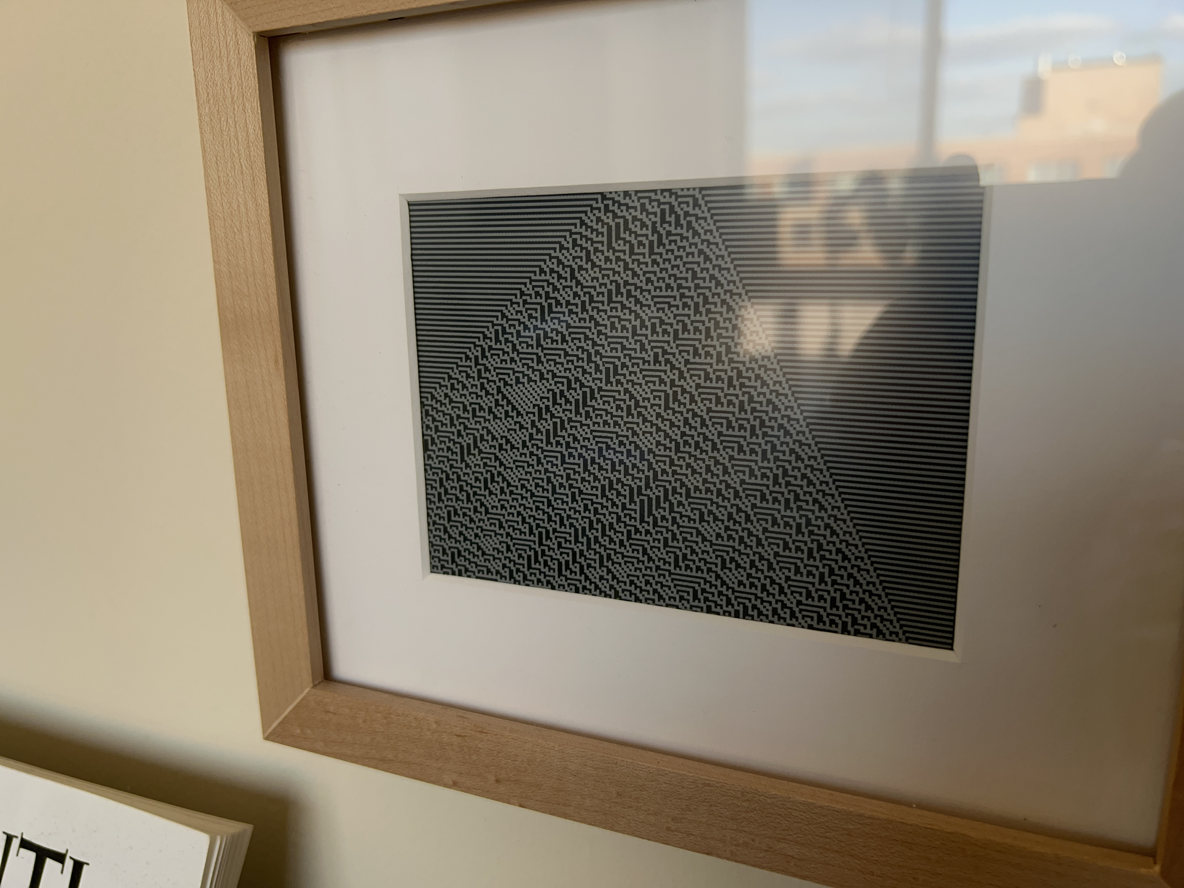 An automata piece on my e-ink screen with a 1” paper border and a wooden frame